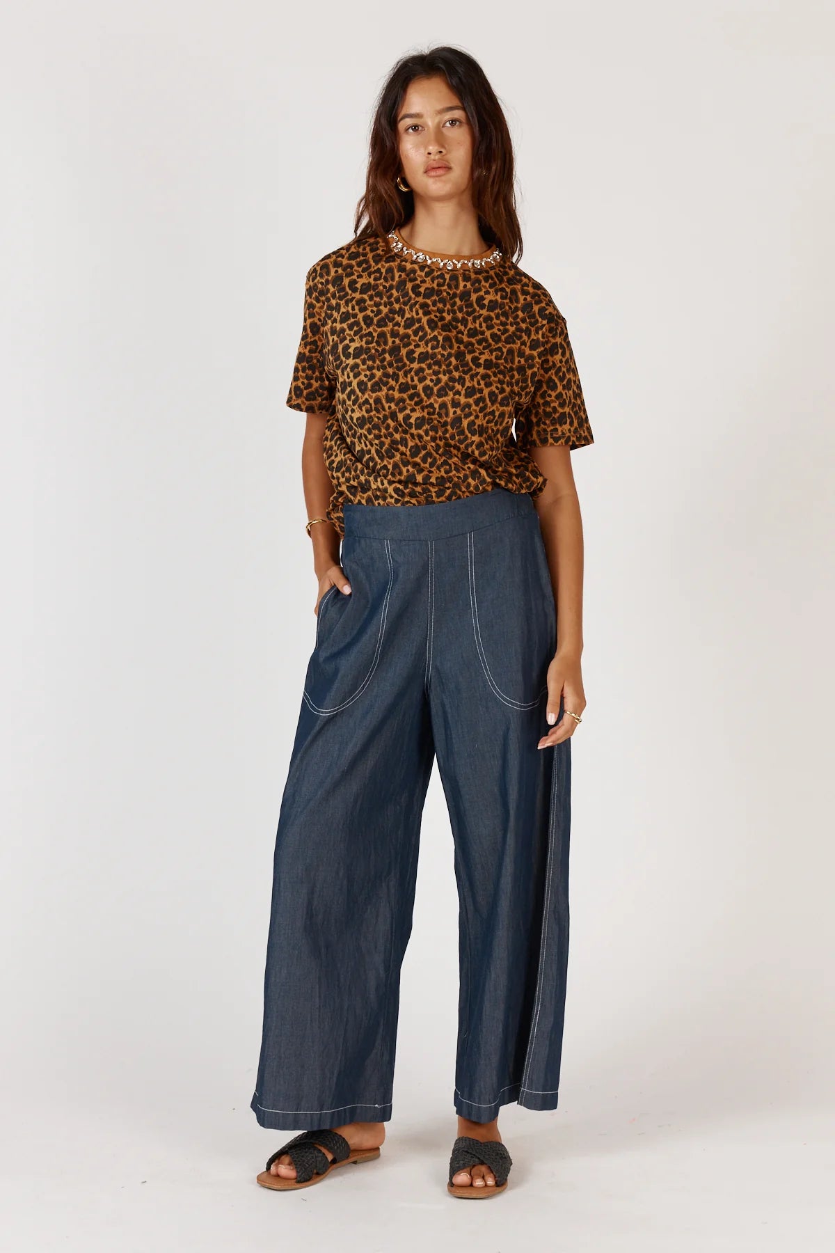 Woman wearing a leopard print top and blue pants on a white background