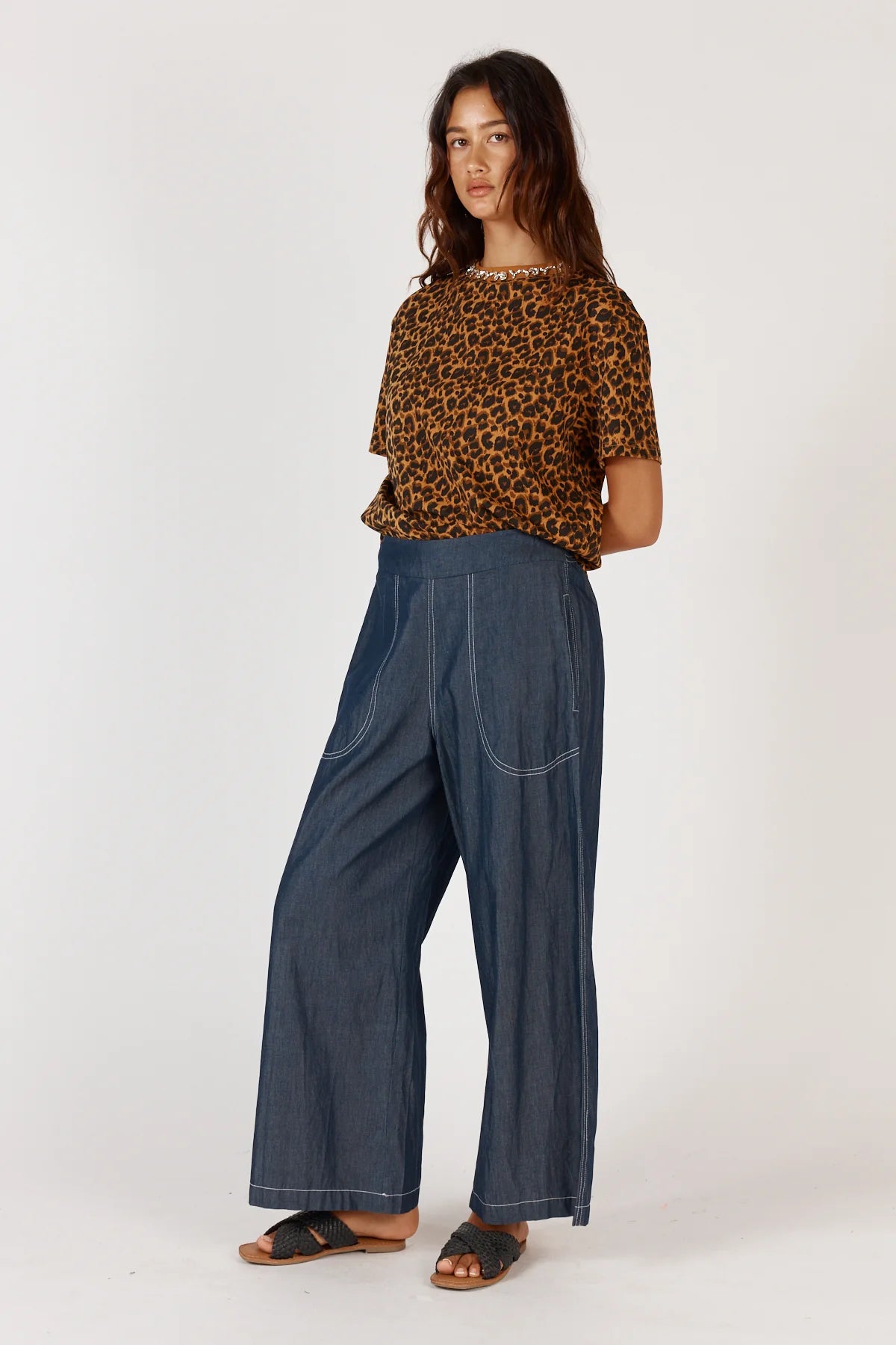 Woman wearing a leopard print top and blue wide-leg pants on a white background