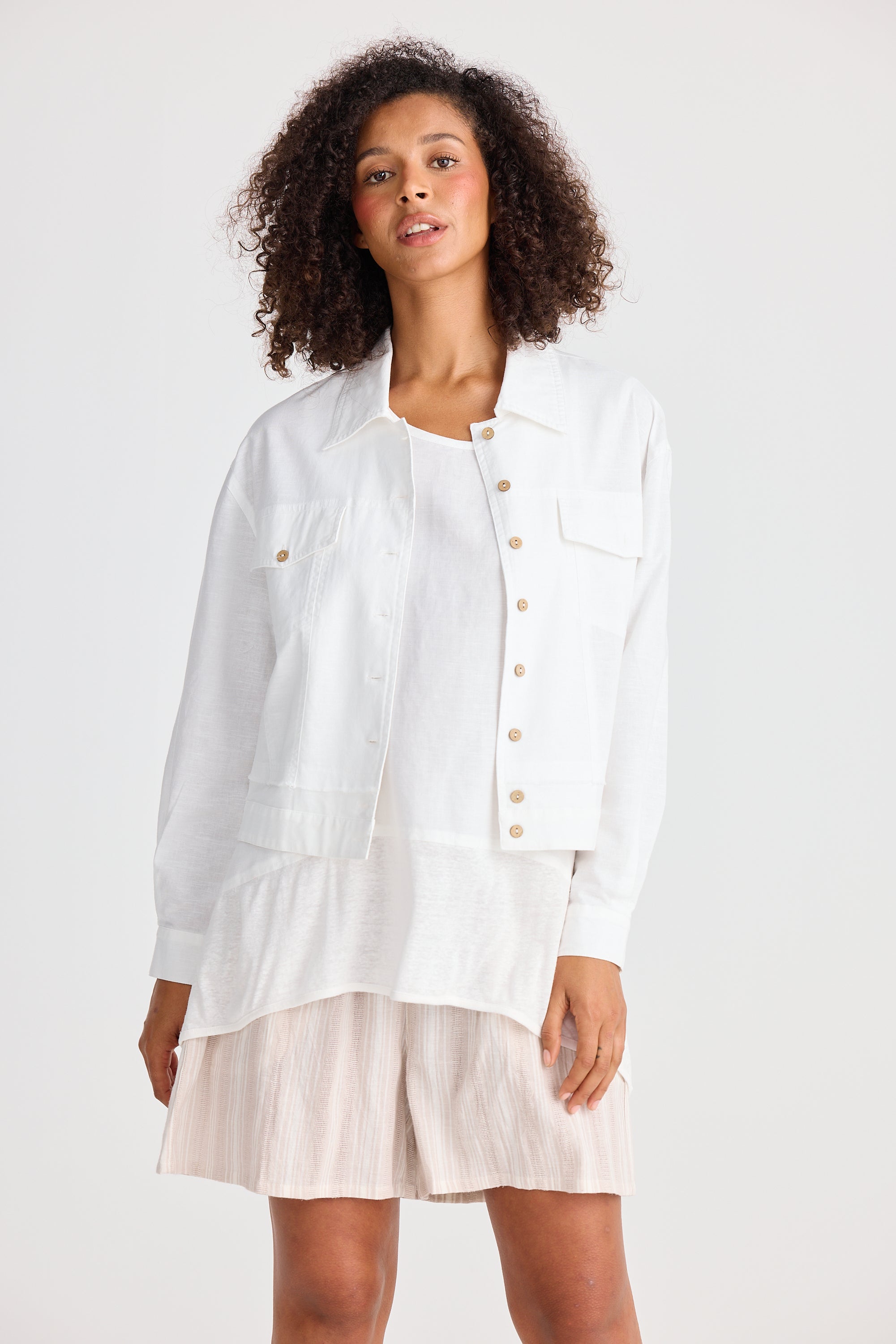 Woman wearing a white button-up shirt and light-colored shorts on a plain background