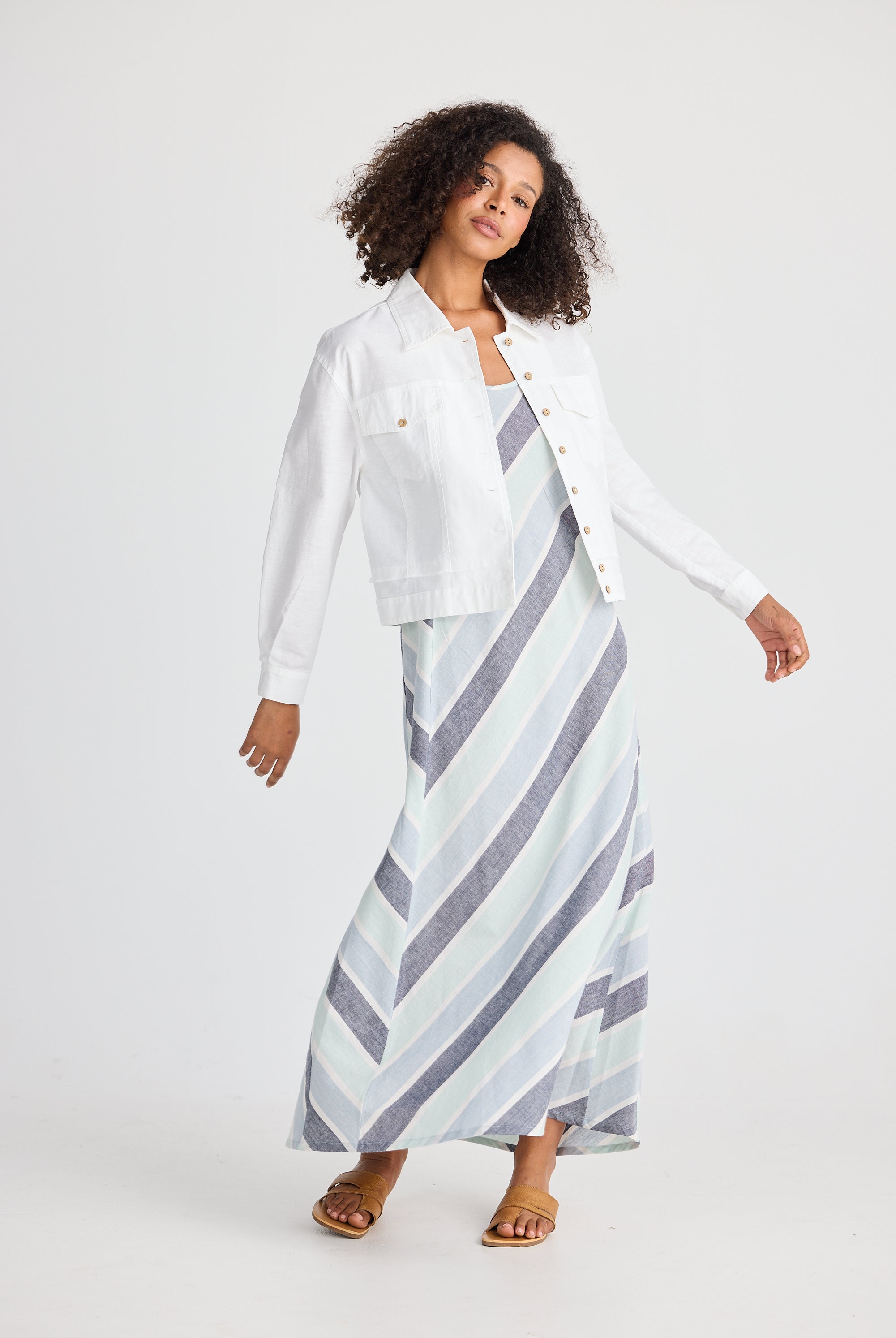 Woman wearing a white jacket and a long, patterned skirt on a plain background