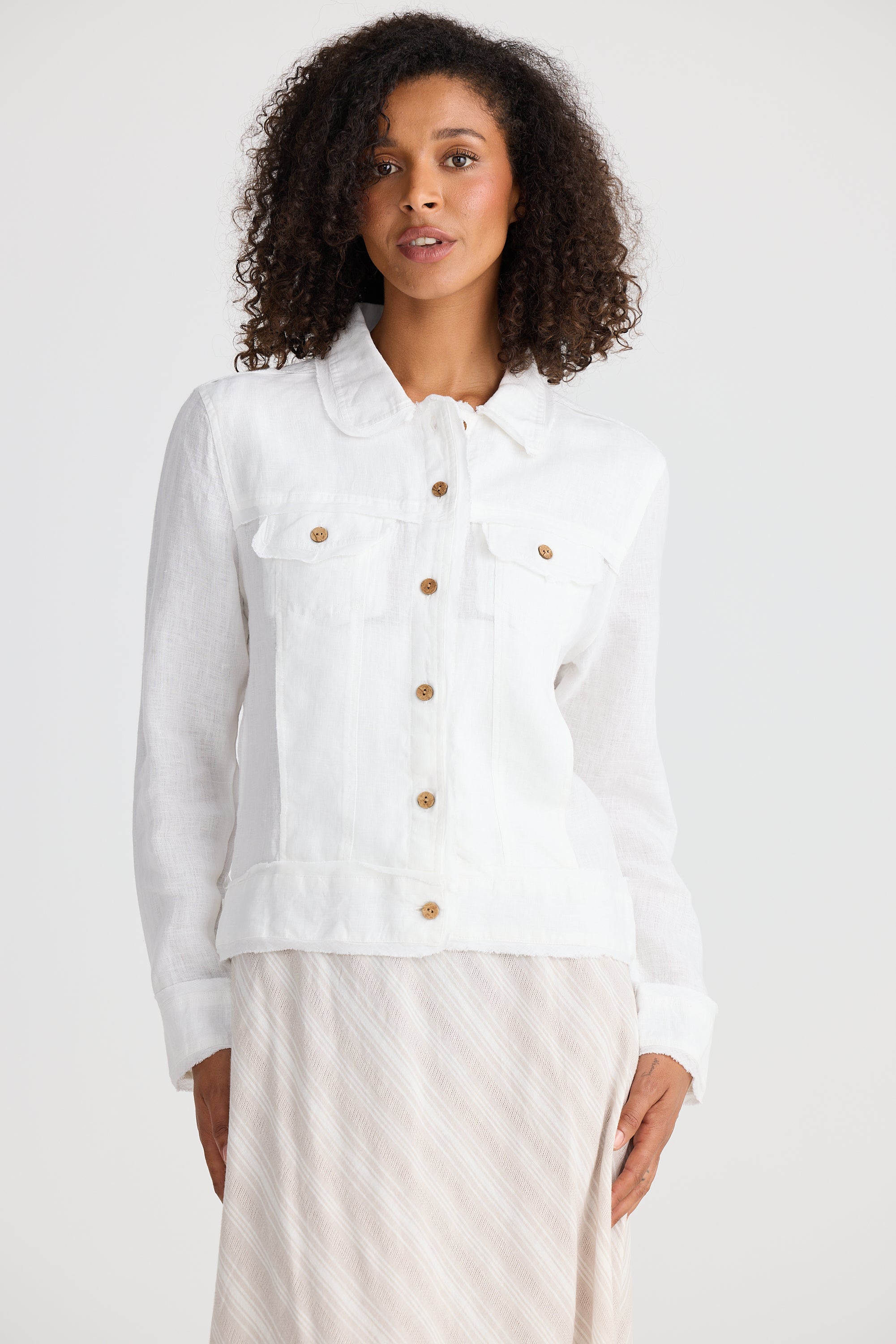 Woman wearing a white jacket with gold buttons on a plain background