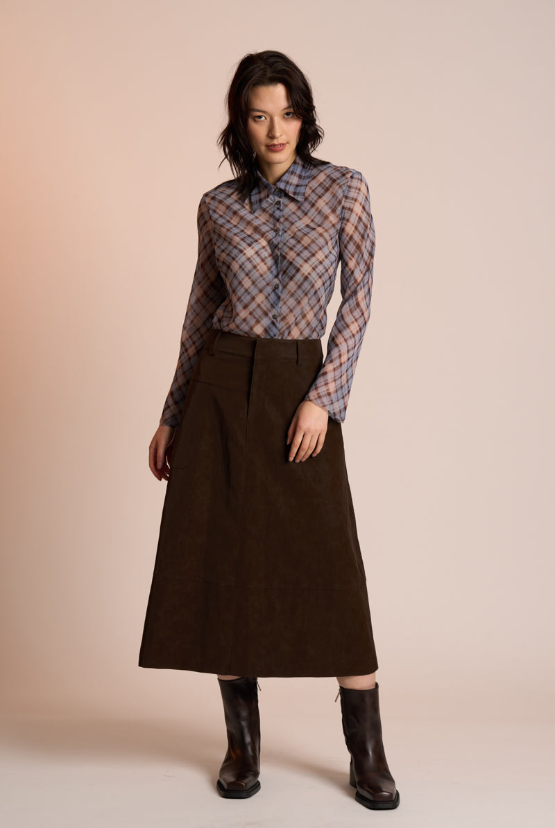 Woman wearing a plaid shirt and brown skirt against a beige background