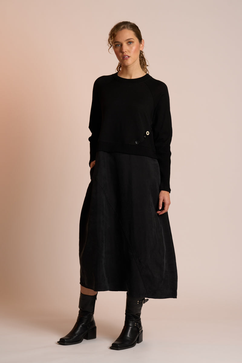 Woman wearing a black outfit with a skirt and boots on a beige background