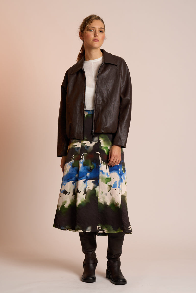 Woman wearing a brown leather jacket and a colorful skirt on a beige background