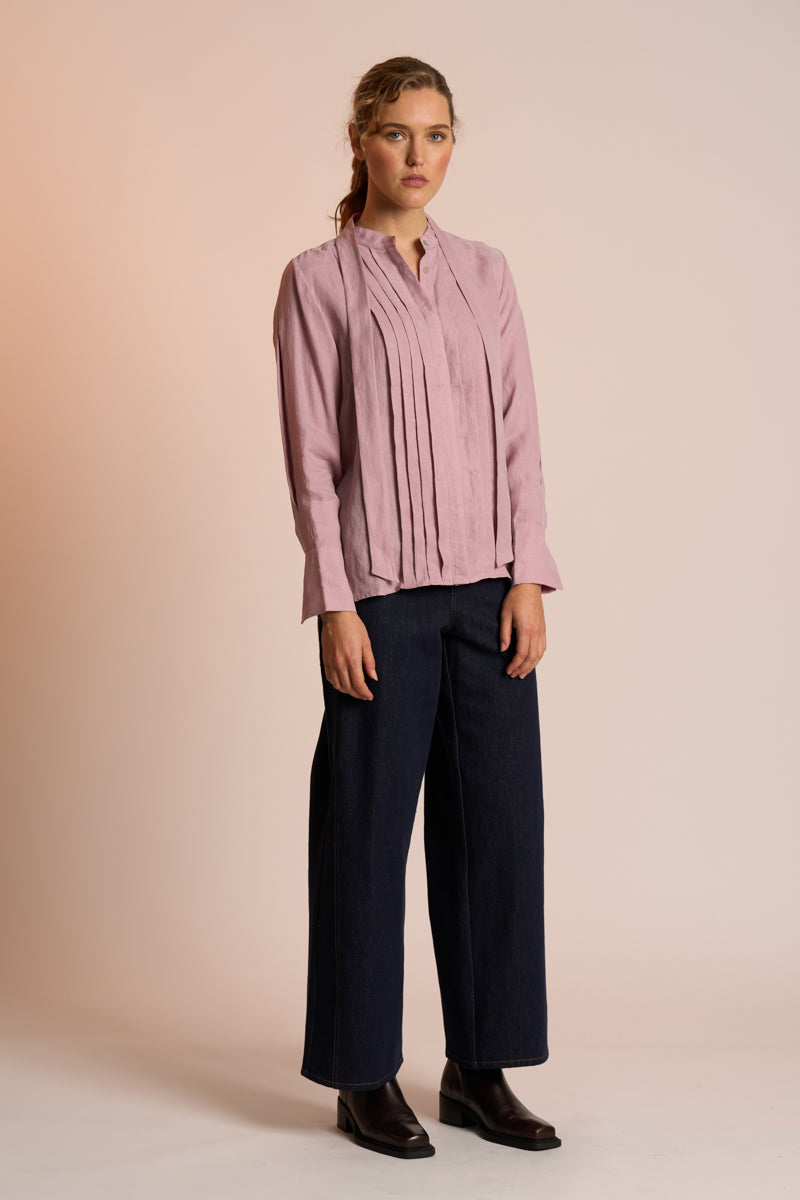 Woman wearing a dusty pink blouse and navy pants against a beige background