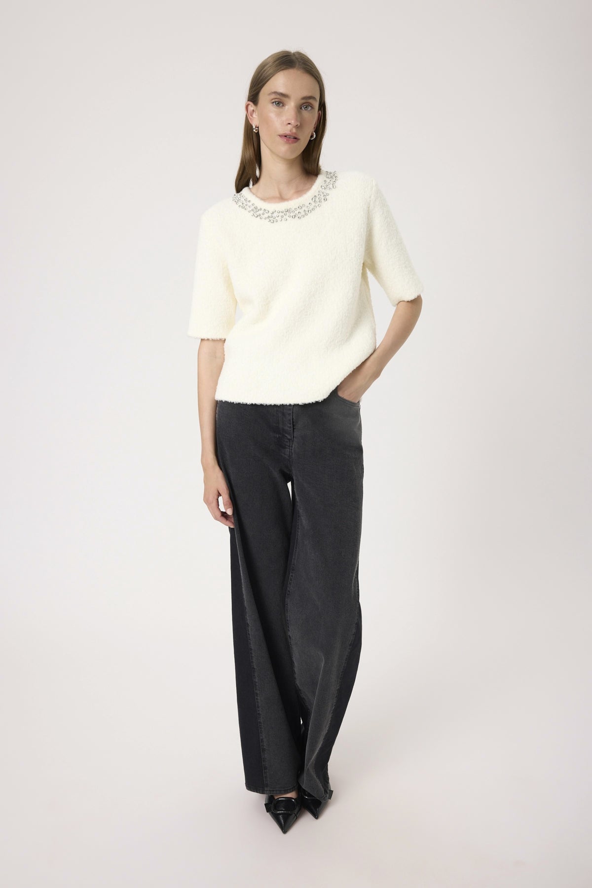Woman wearing a white sweater with embellishments and black wide-leg pants on a white background