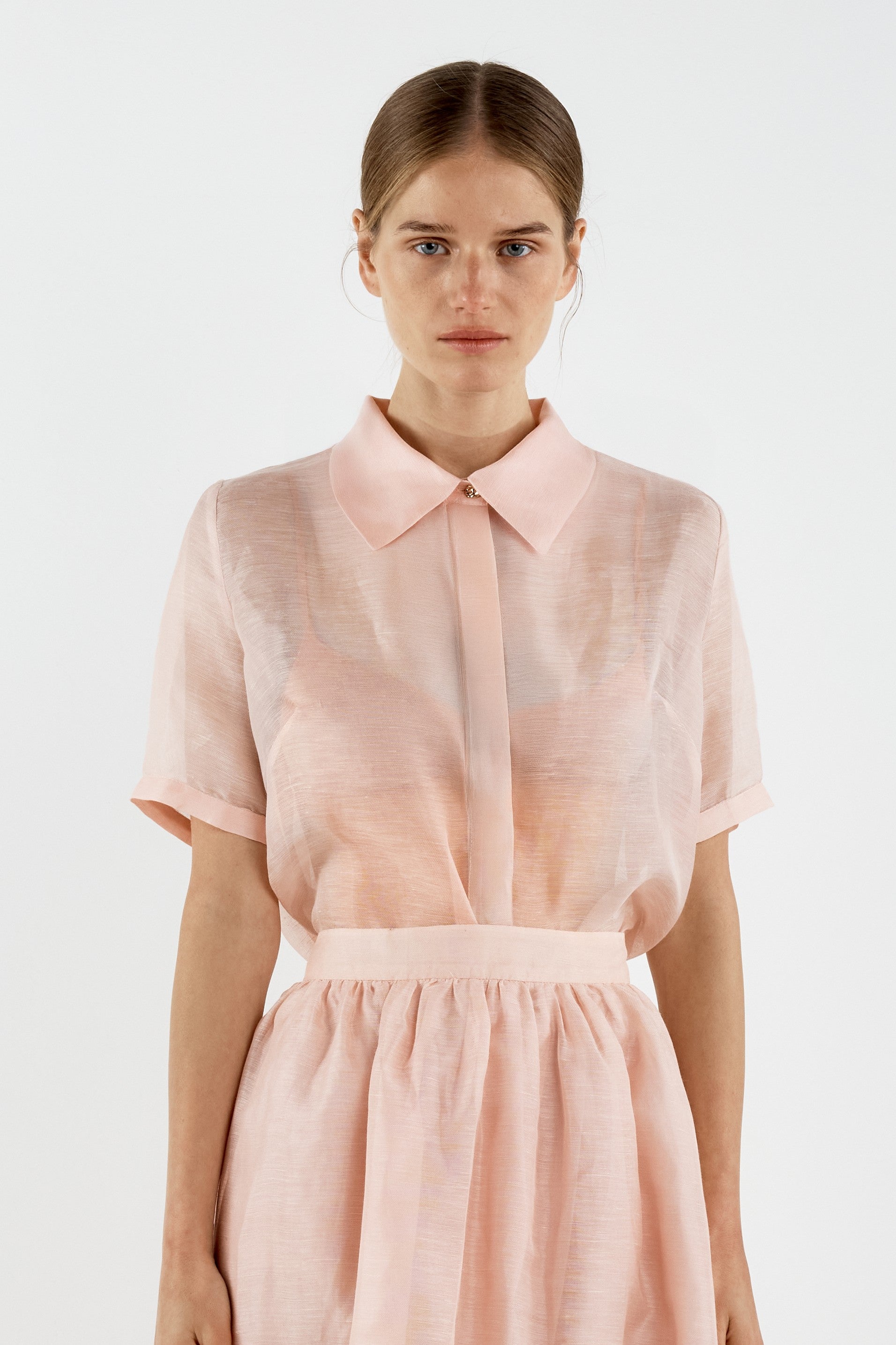 Woman wearing a light pink shirt with a collar on a white background