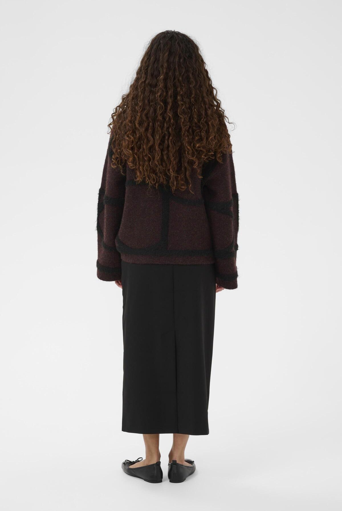 Person wearing a dark burgundy sweater and black skirt on a white background