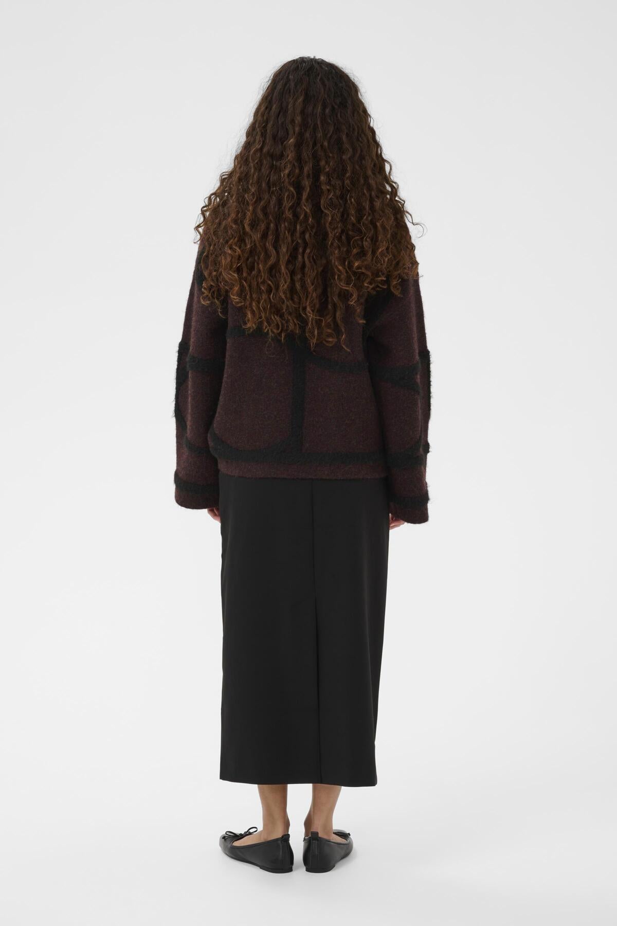 Person wearing a dark burgundy sweater and black skirt on a white background
