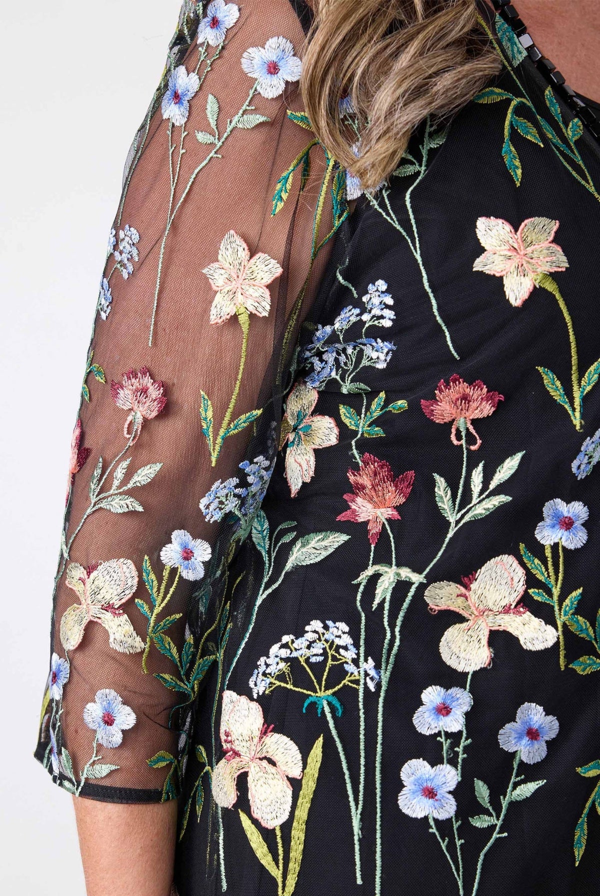Close-up of a black embroidered sheer mesh top with multicolored floral patterns, featuring a model's arm and shoulder.