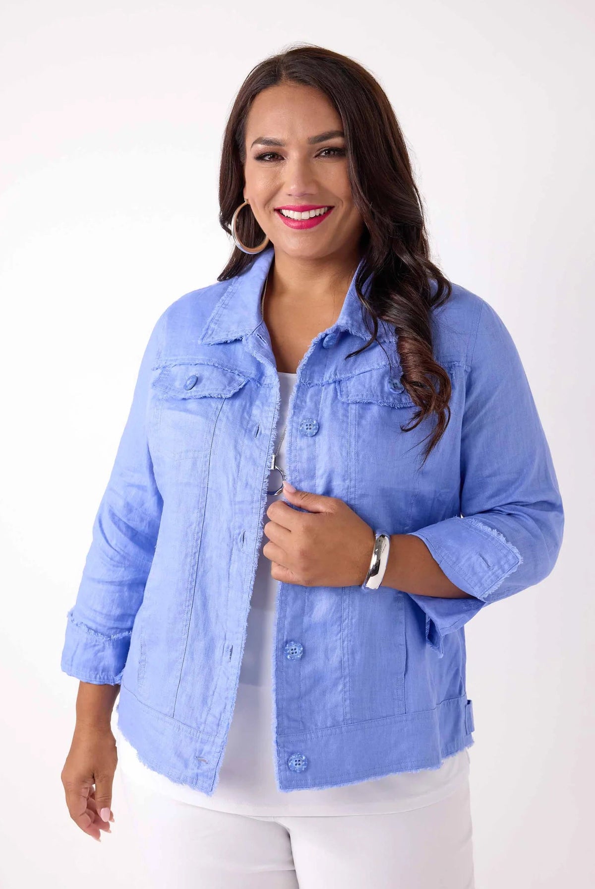 A woman modeling a light blue cropped denim jacket over a white top and white pants, standing against a plain white studio background.