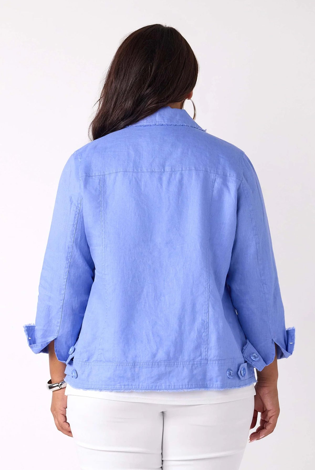 A woman viewed from the back wearing a light blue cropped jacket with rolled sleeves and white pants, against a plain white studio background.
