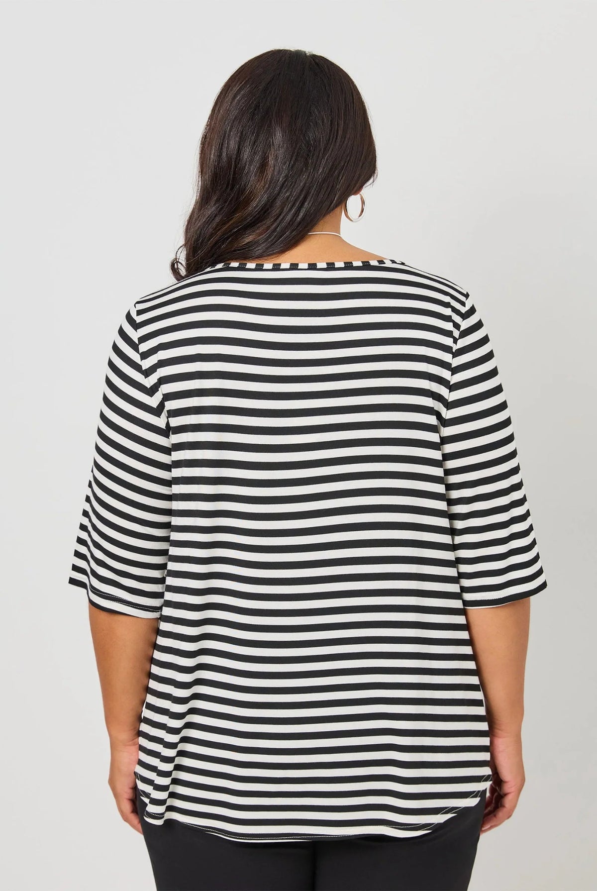 A woman viewed from the back wearing a black and white horizontally striped short-sleeve top, set against a plain light gray studio background.