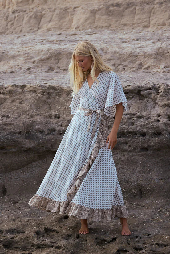 Woman in a long dress standing on rocky terrain with a cliff in the background