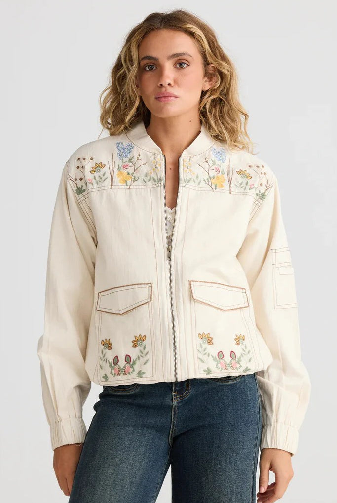 Woman wearing a cream-colored embroidered jacket on a plain background
