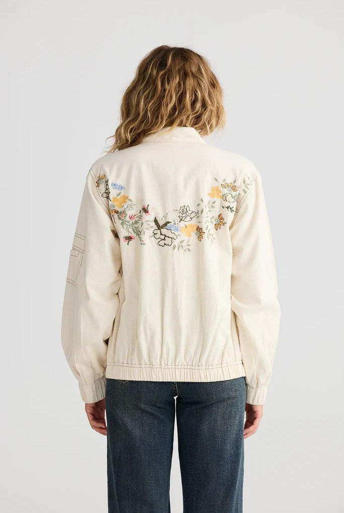 Person wearing a cream-colored jacket with floral embroidery on the back against a white background