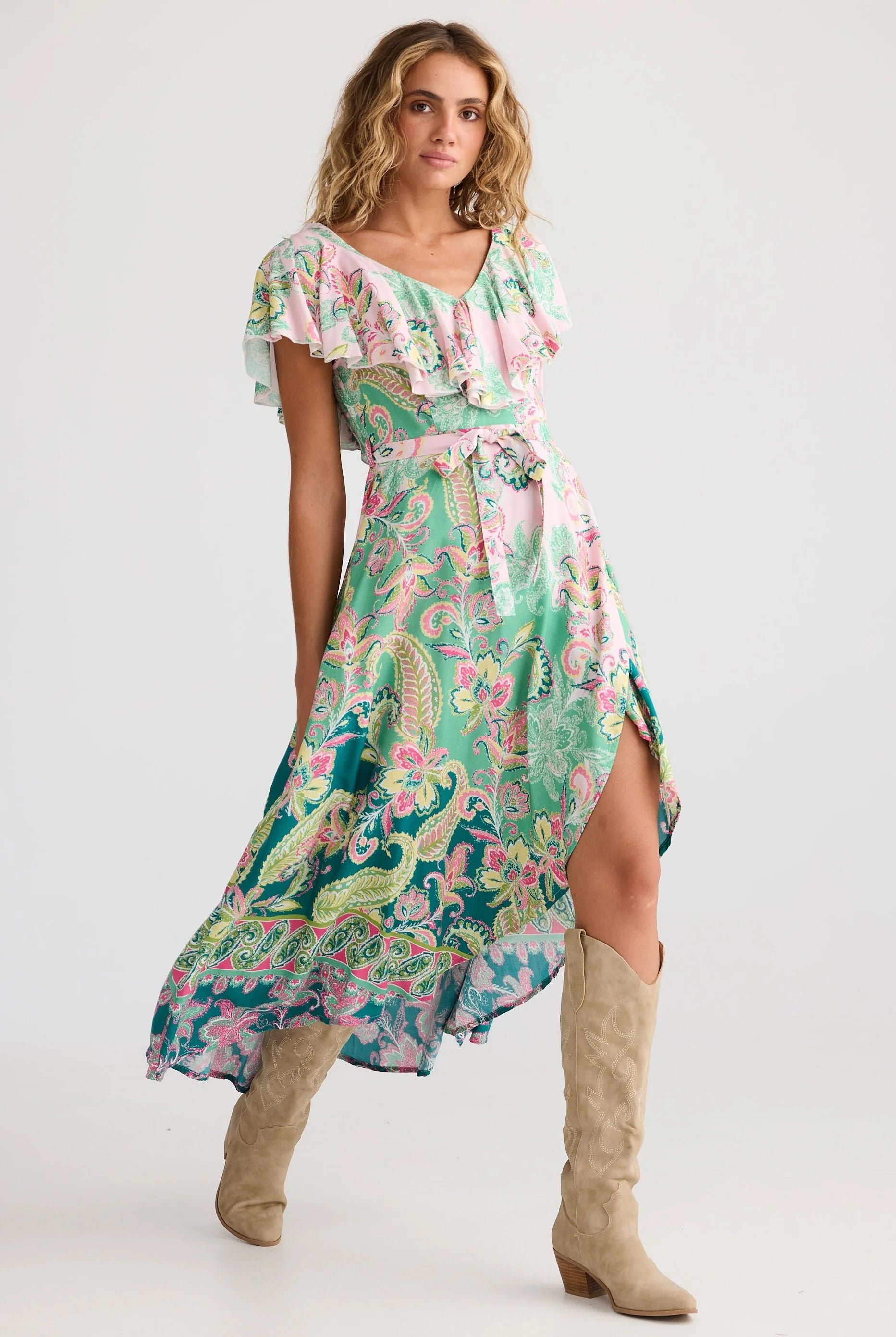 Woman wearing a floral dress with a high-low hem and knee-high boots on a white background