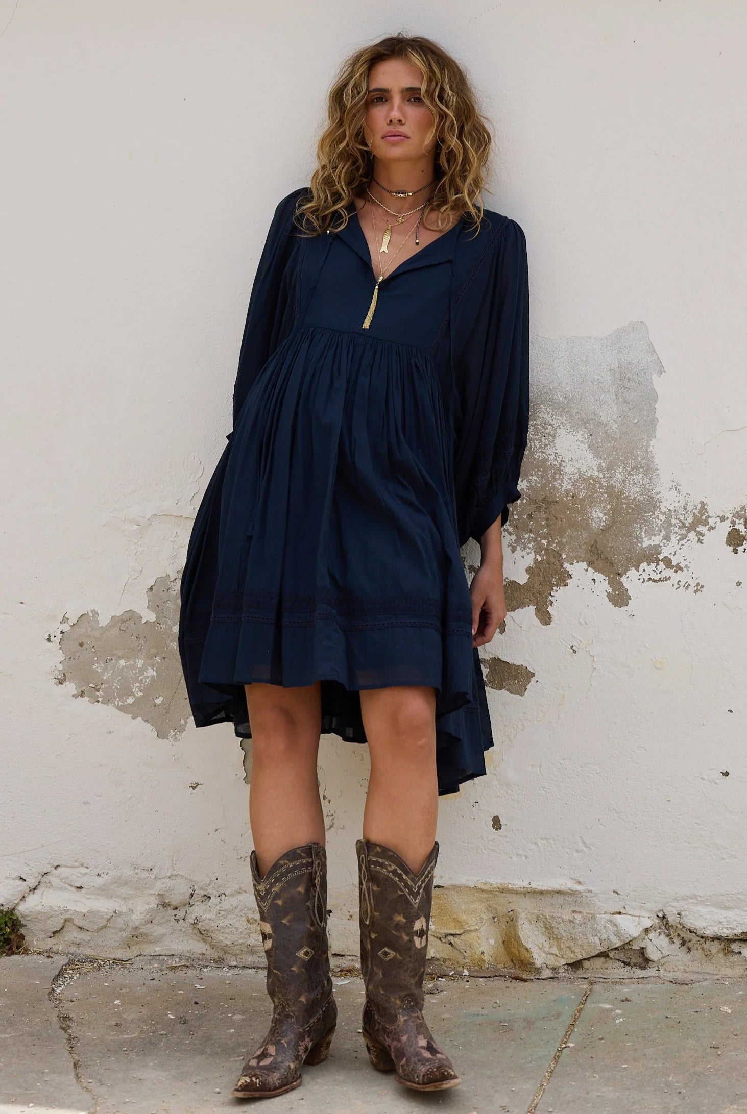 Woman wearing a navy dress and brown boots against a textured wall.