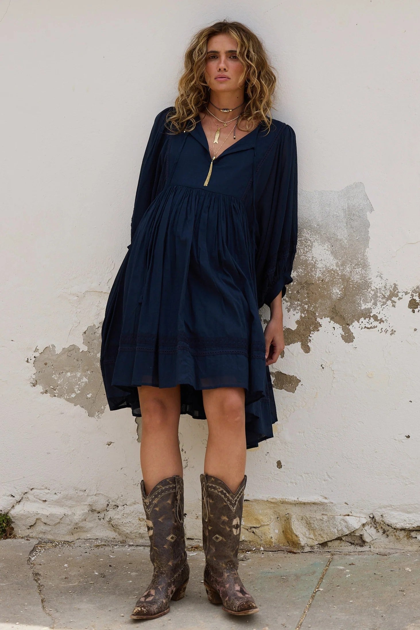 Woman wearing a navy dress and brown boots against a textured wall.
