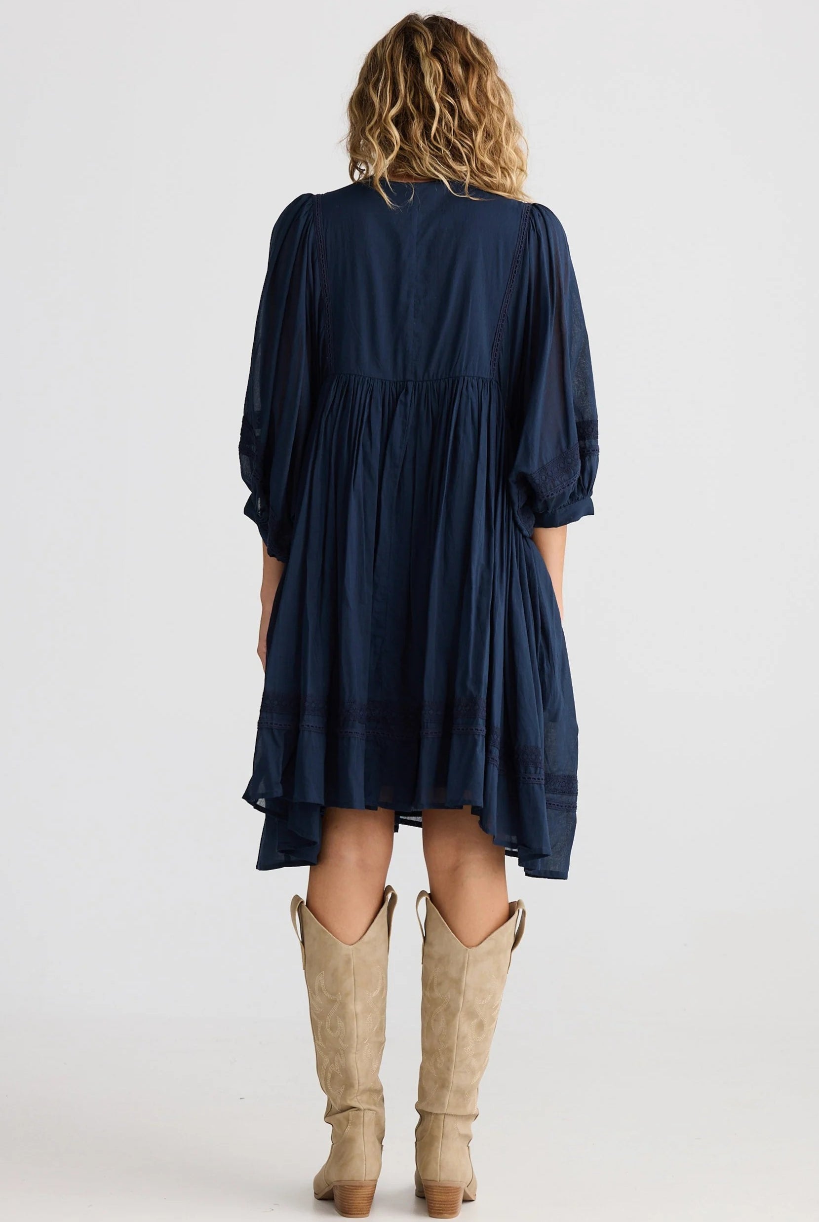 Person wearing a navy dress with long sleeves and a white background back