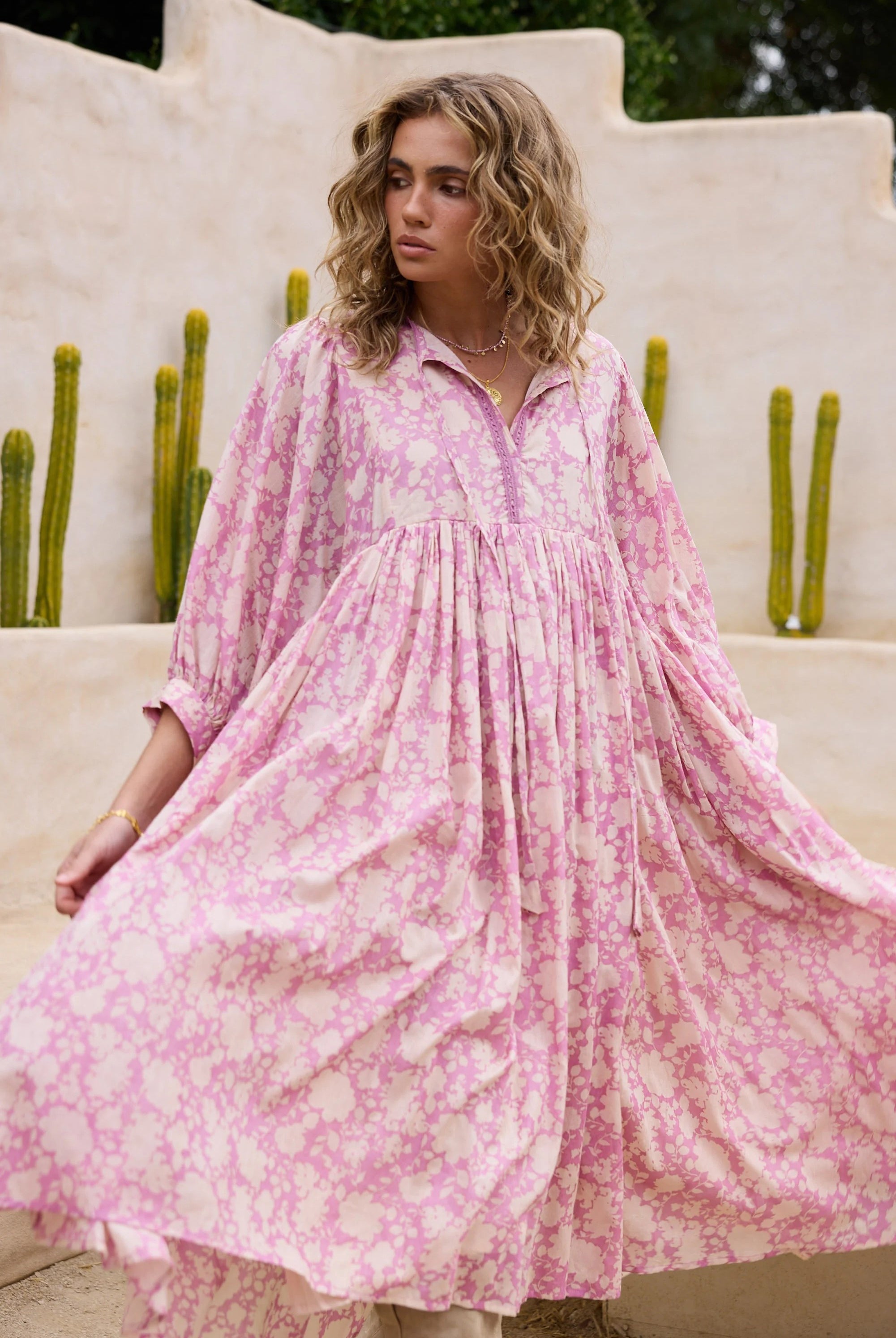 Woman wearing a pink floral dress standing outdoors with cacti in the background