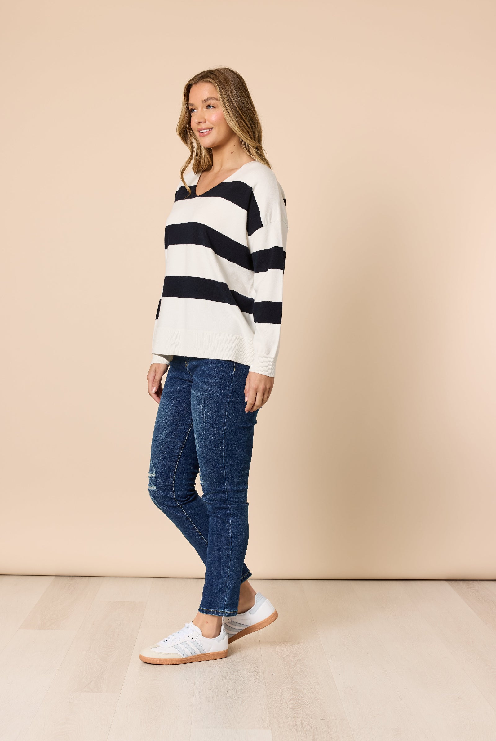 Woman wearing a black and white striped sweater and blue jeans against a beige background