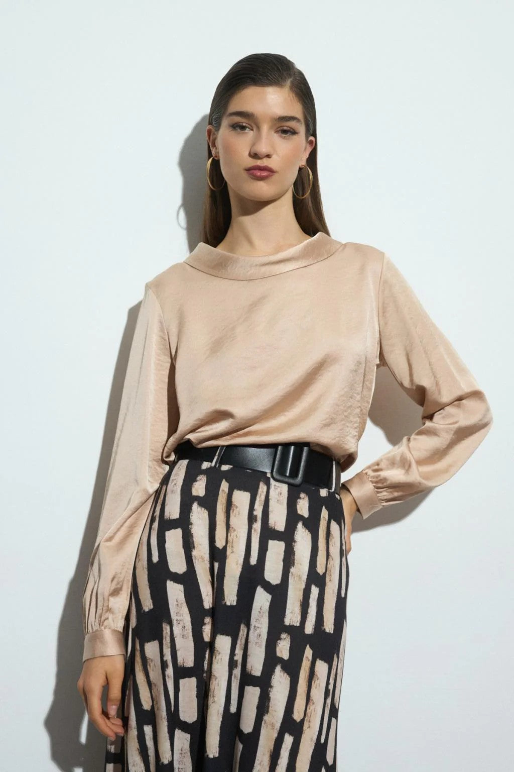 Woman wearing a beige long-sleeve blouse and patterned skirt against a white background