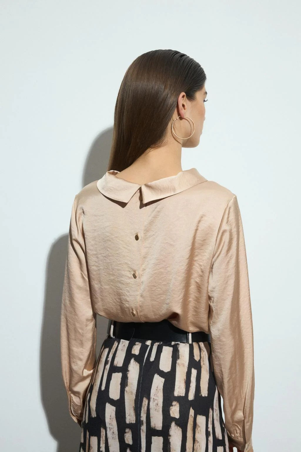 Woman wearing a beige long-sleeve blouse and patterned skirt against a white background back angle