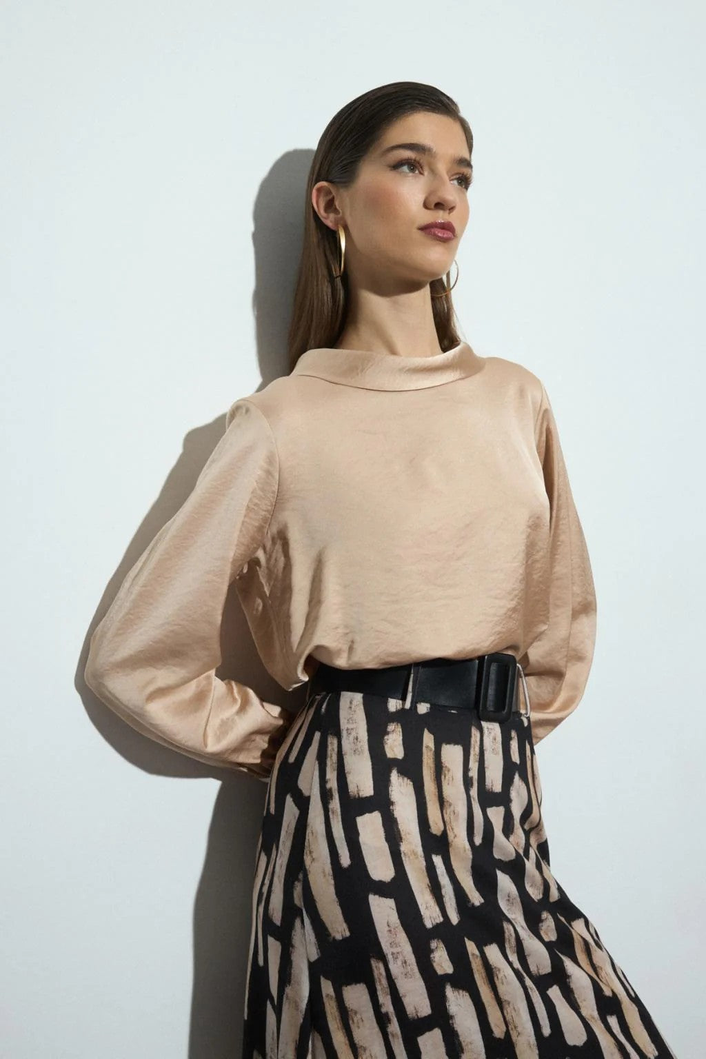 Woman wearing a beige long-sleeve blouse and patterned skirt against a white background