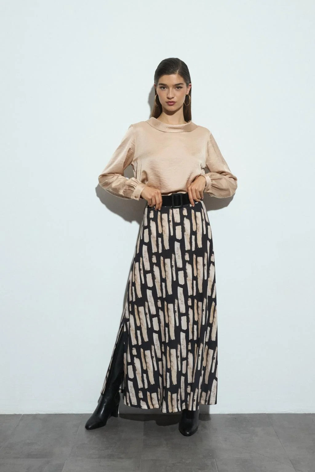 Woman wearing a beige long-sleeve blouse and patterned skirt against a white background