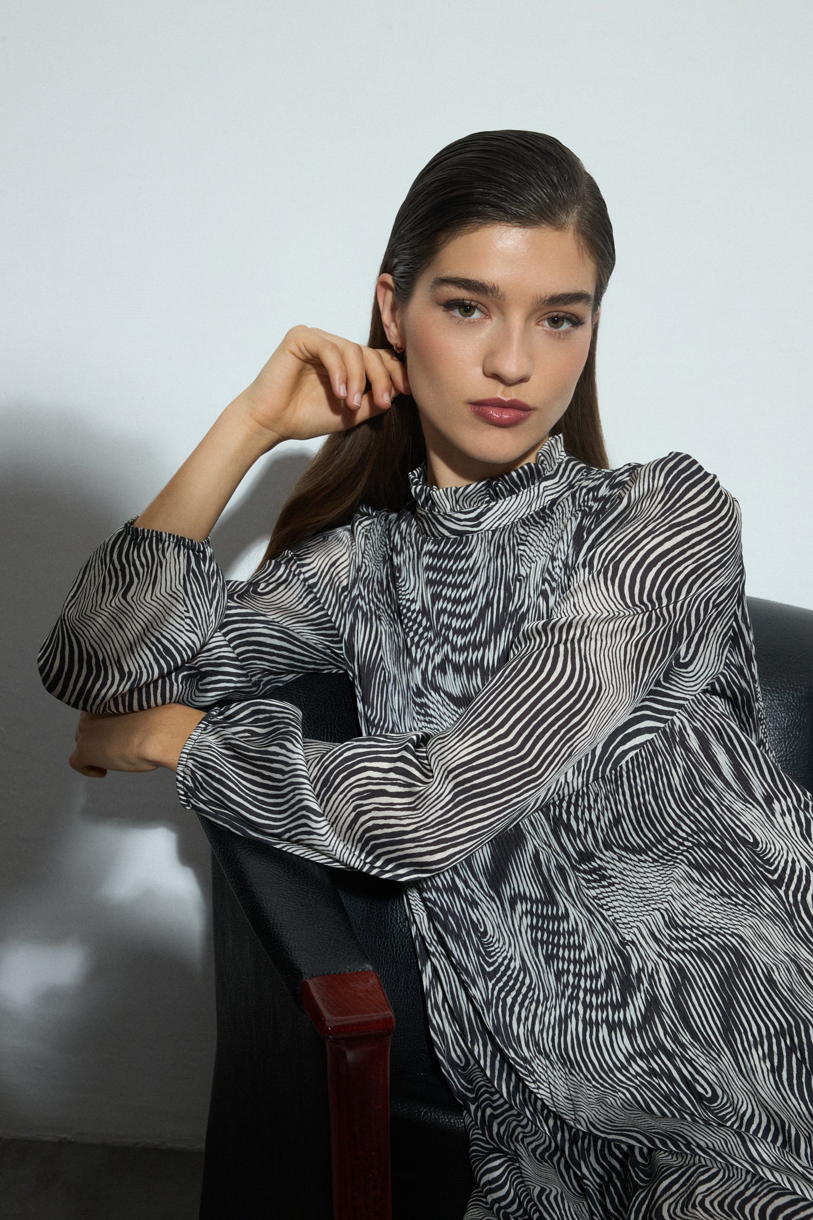 Woman wearing a patterned dress sitting on a chair against a plain background