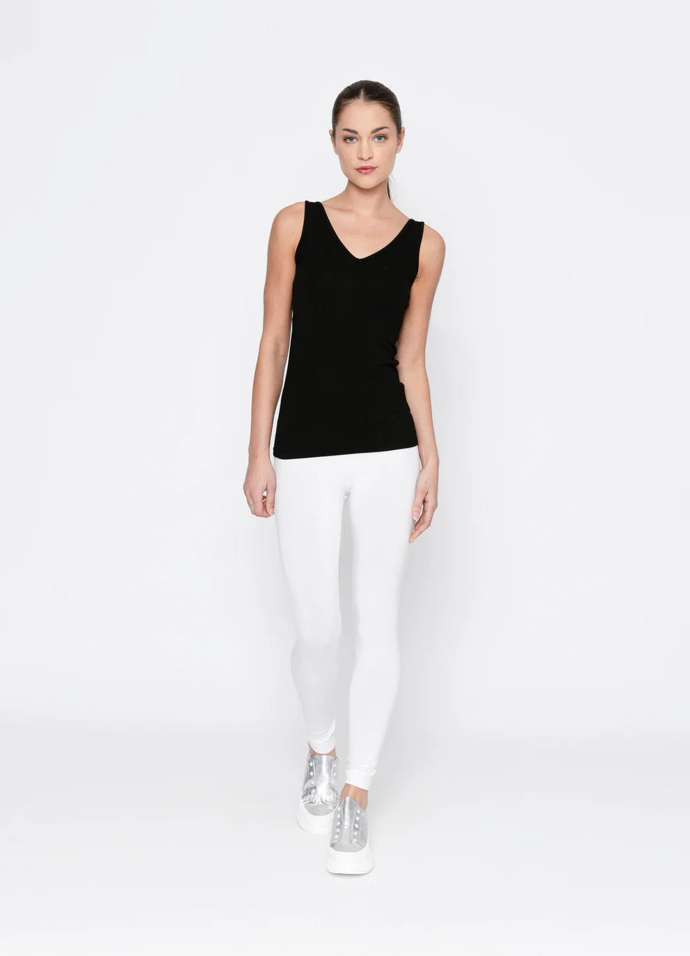 Woman wearing a black sleeveless top and white pants on a white background