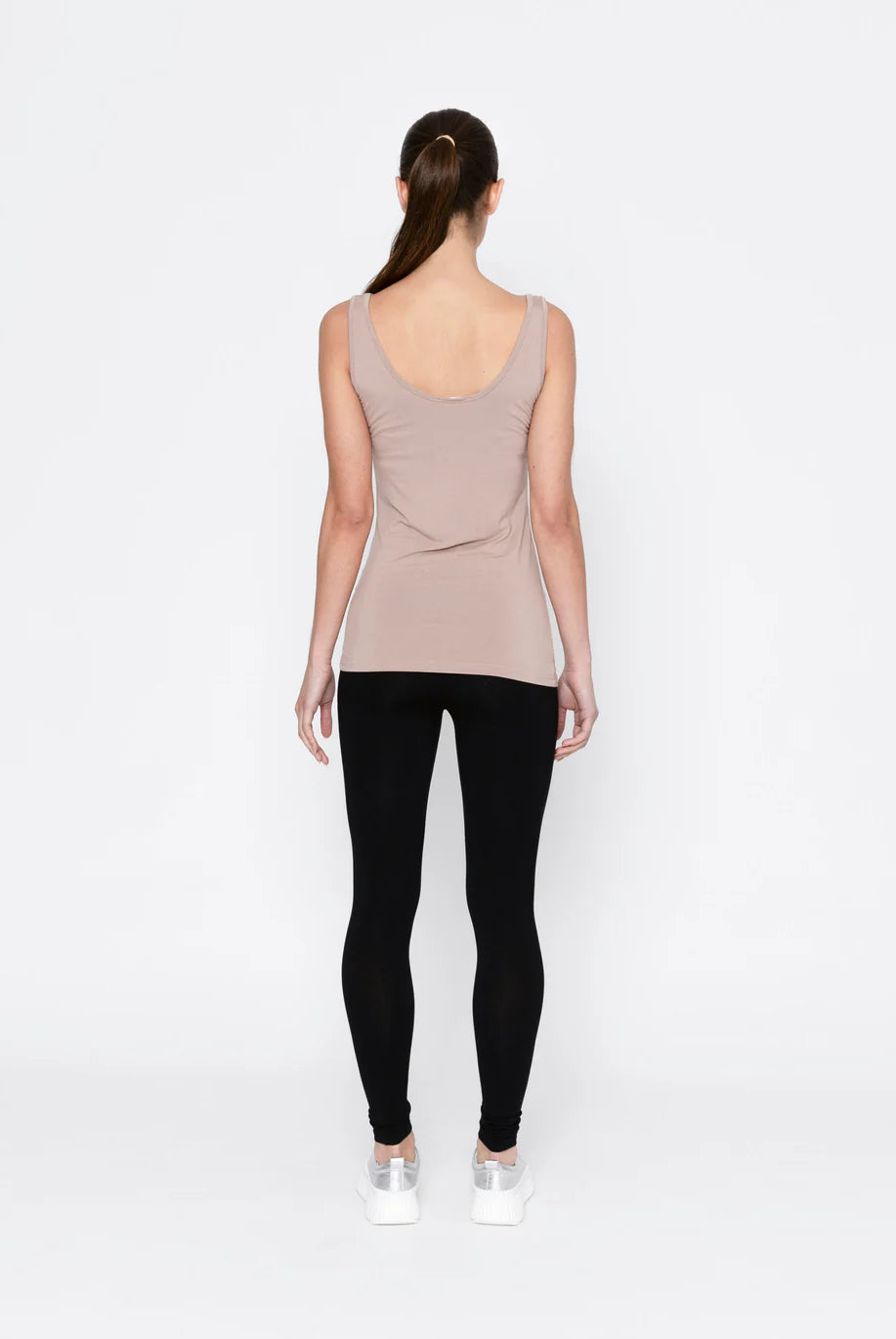 Person wearing a beige tank top and black leggings on a white background