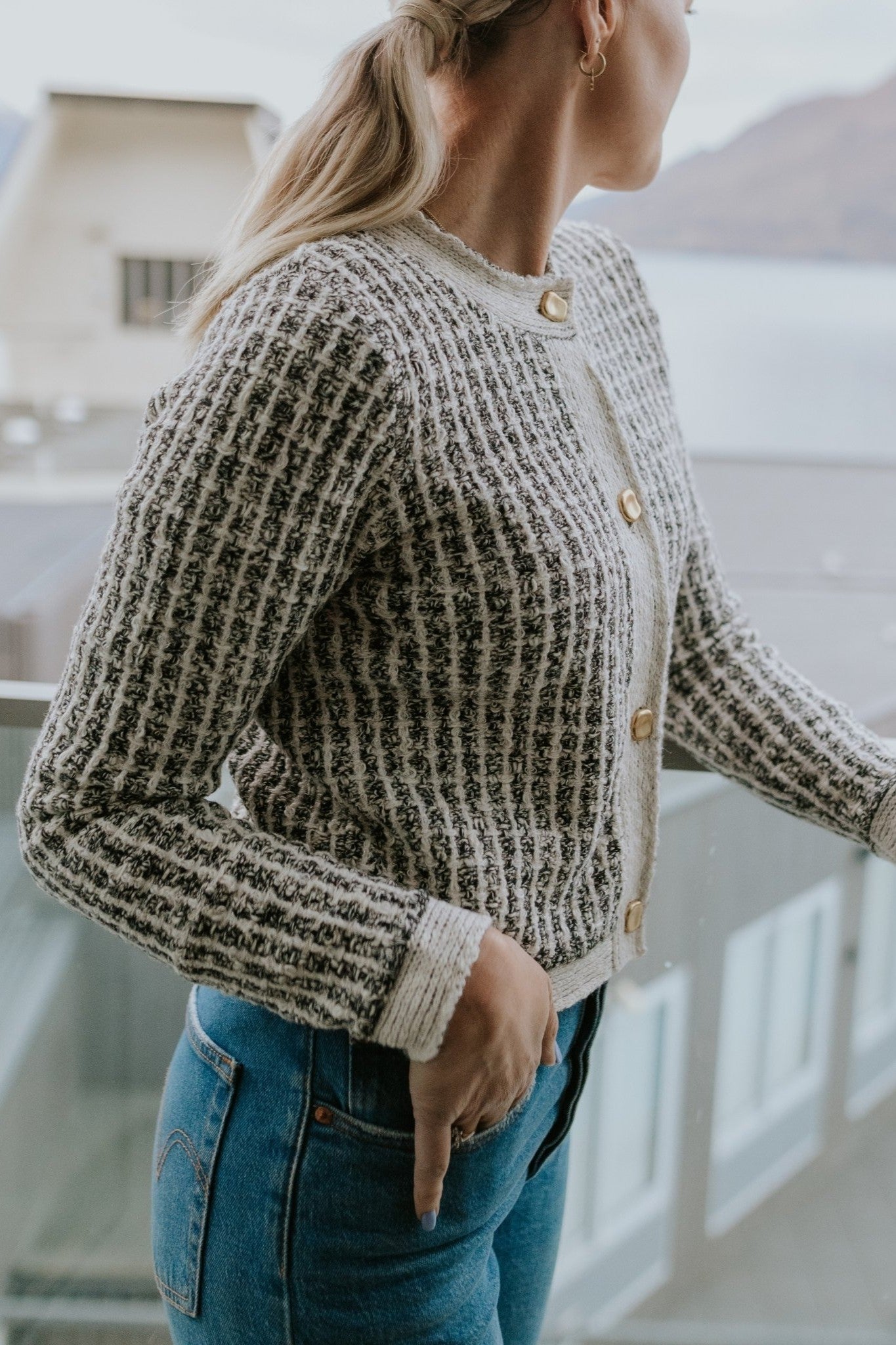 Woman wearing cream check cardigan and blue jeans standing on balcony
