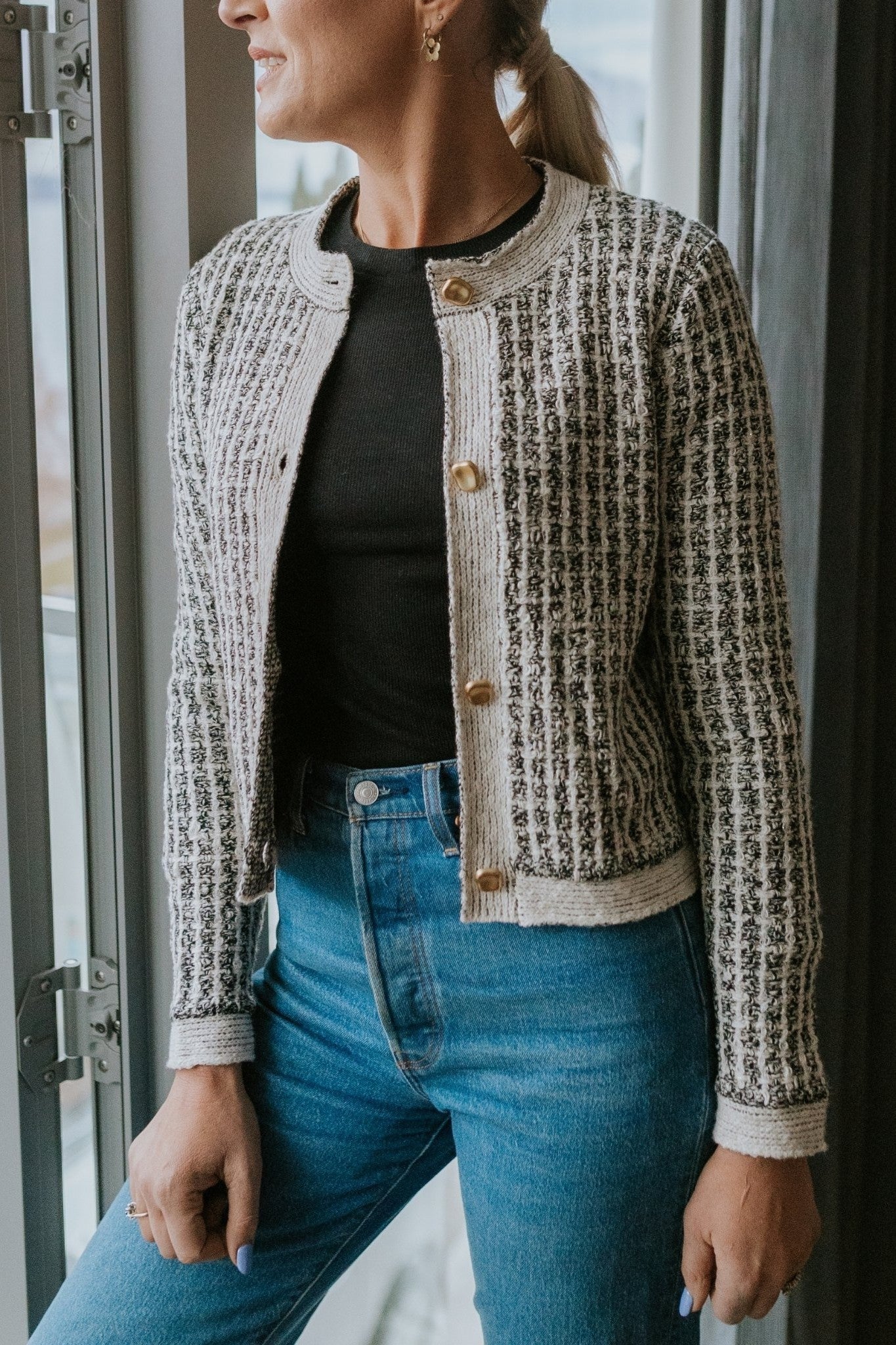 Woman wearing cream check cardigan over black top and blue jeans