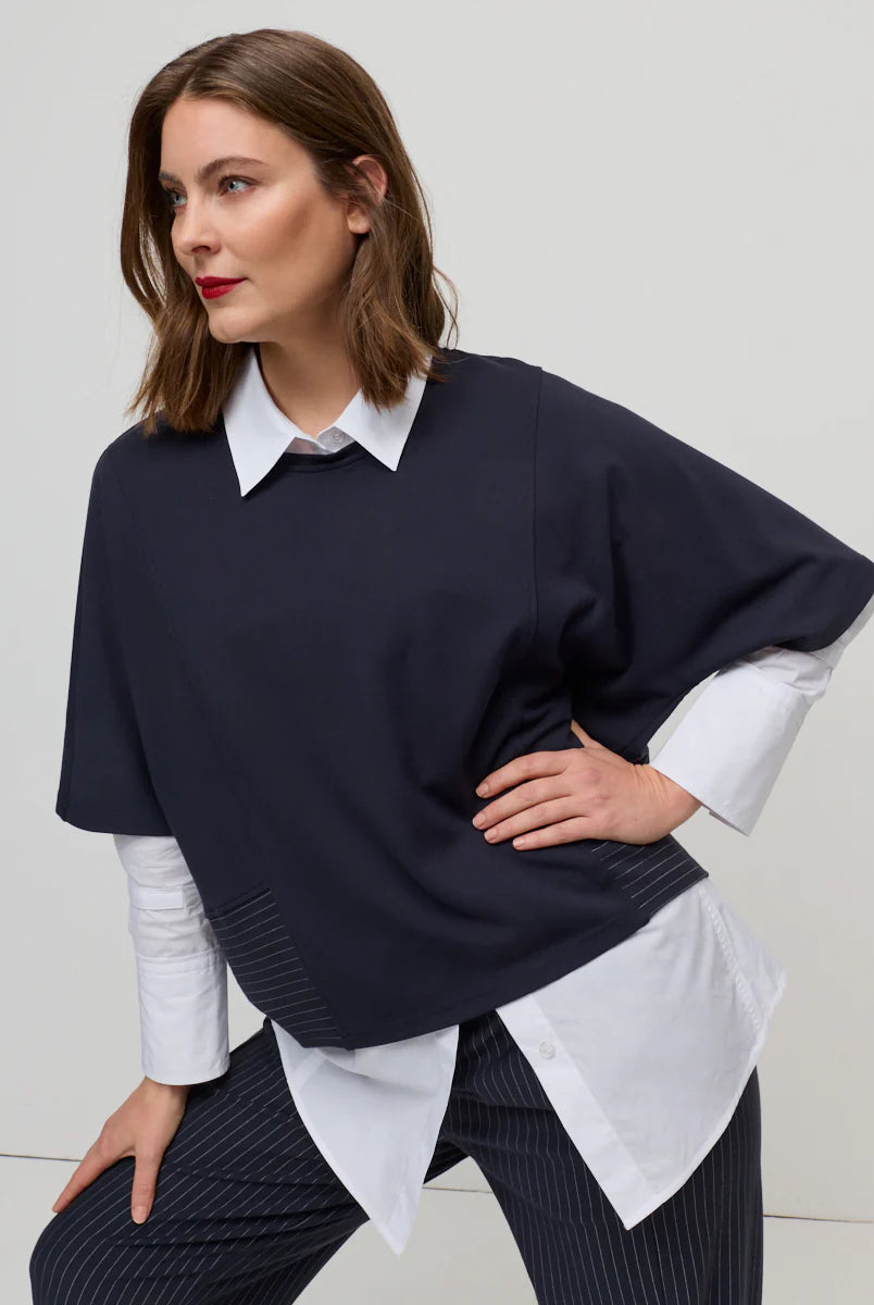 Woman wearing a navy sweater over a white shirt with a plain background