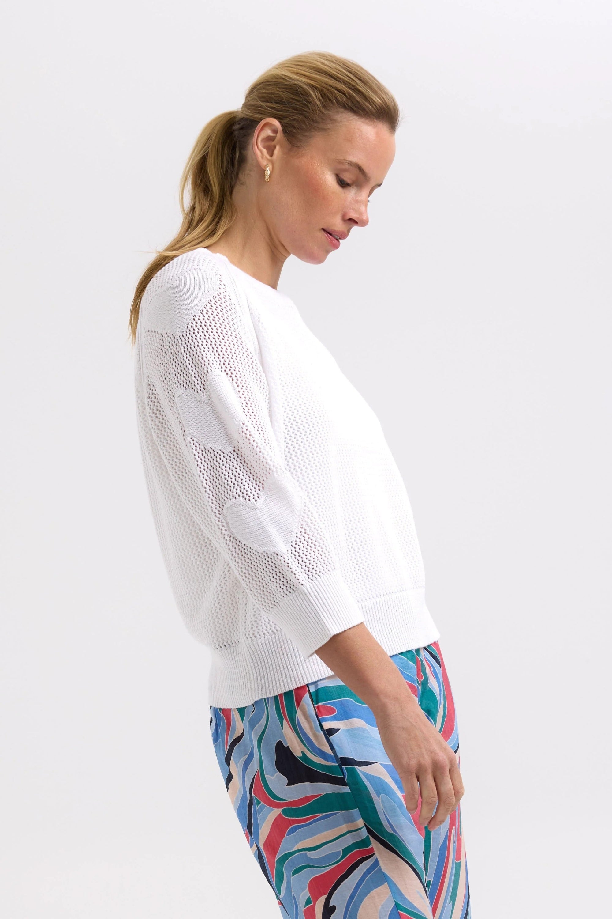 Woman wearing a white sweater and colorful pants on a light gray background