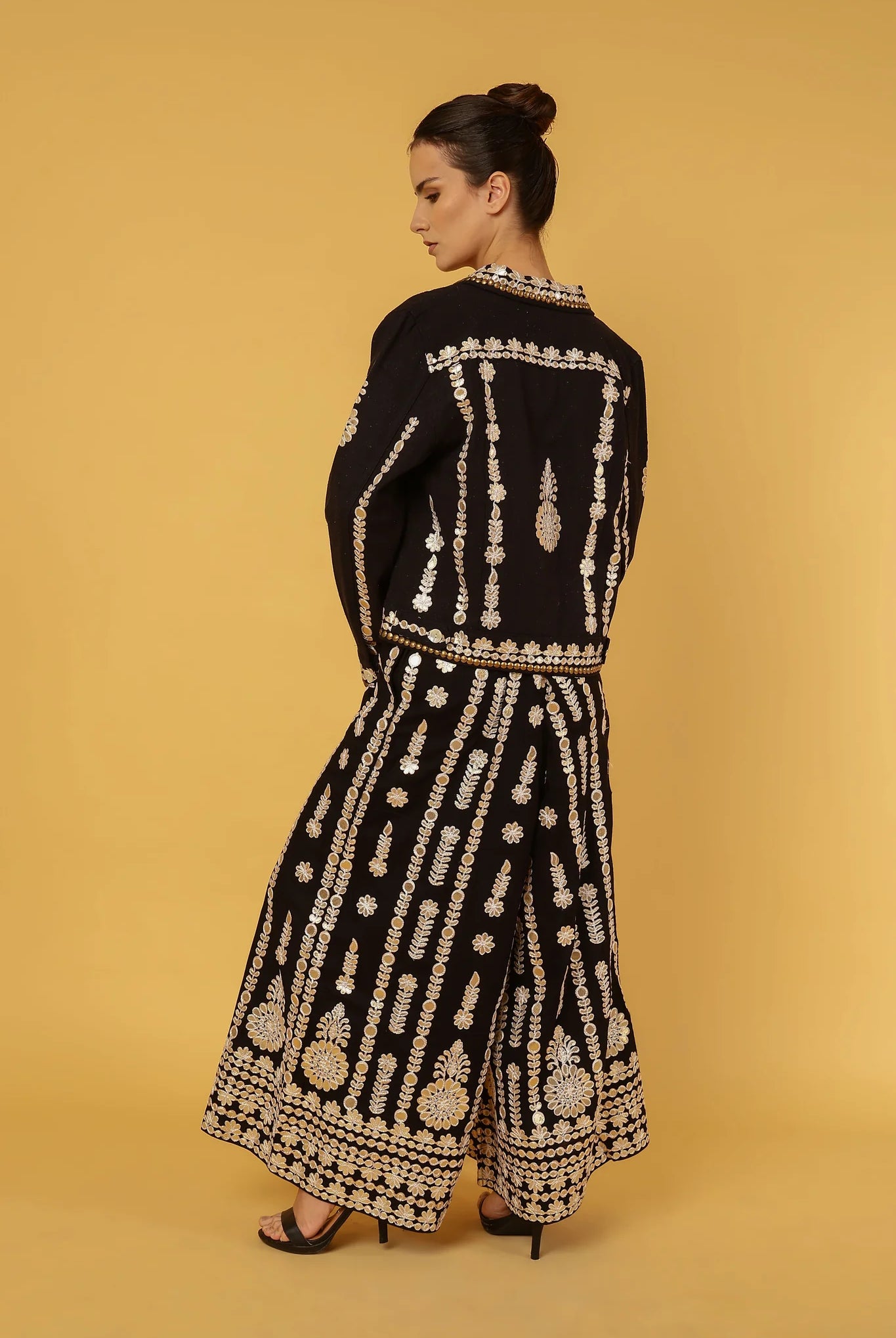 Woman wearing a black outfit with gold embroidery and mirrors on a beige background