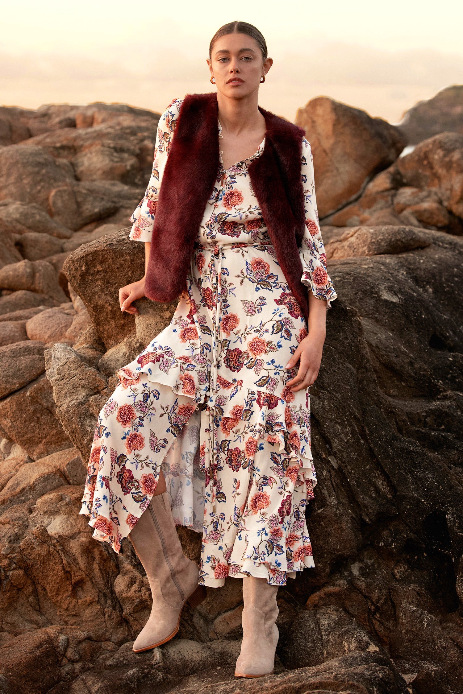 Woman in a floral dress and fur vest standing on rocky terrain