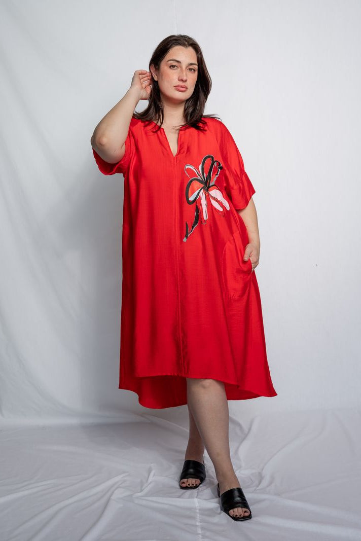 Woman wearing a v neck bright red midi length dress with elbow length sleeves and flower motif against a white background.