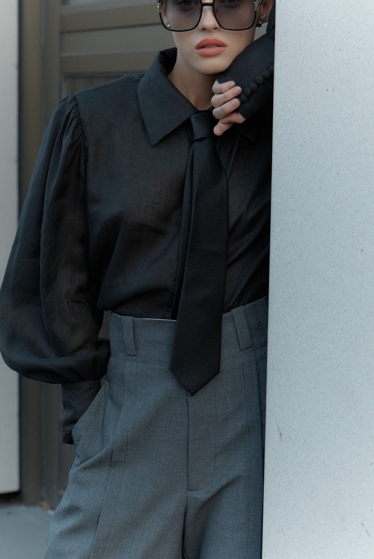 Person wearing a black shirt and gray pants peeking from behind a white wall.