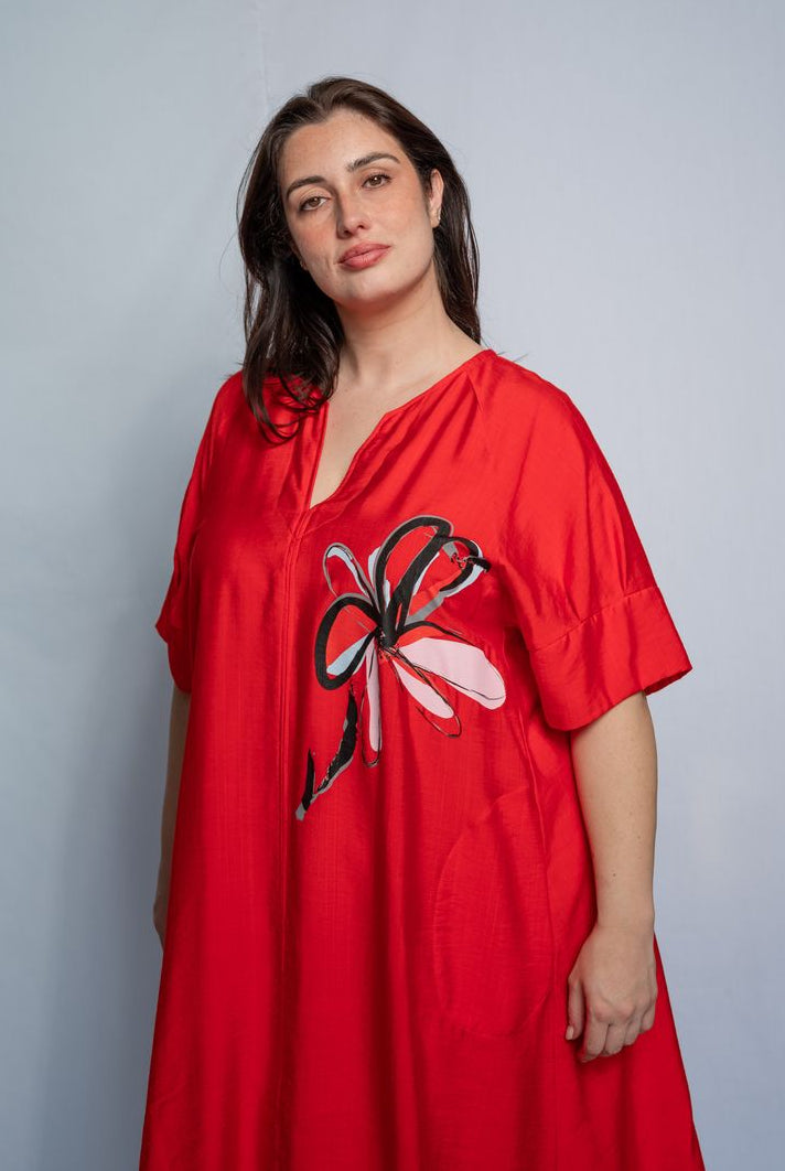Woman wearing a v neck bright red midi length dress with elbow length sleeves and flower motif against a white background.