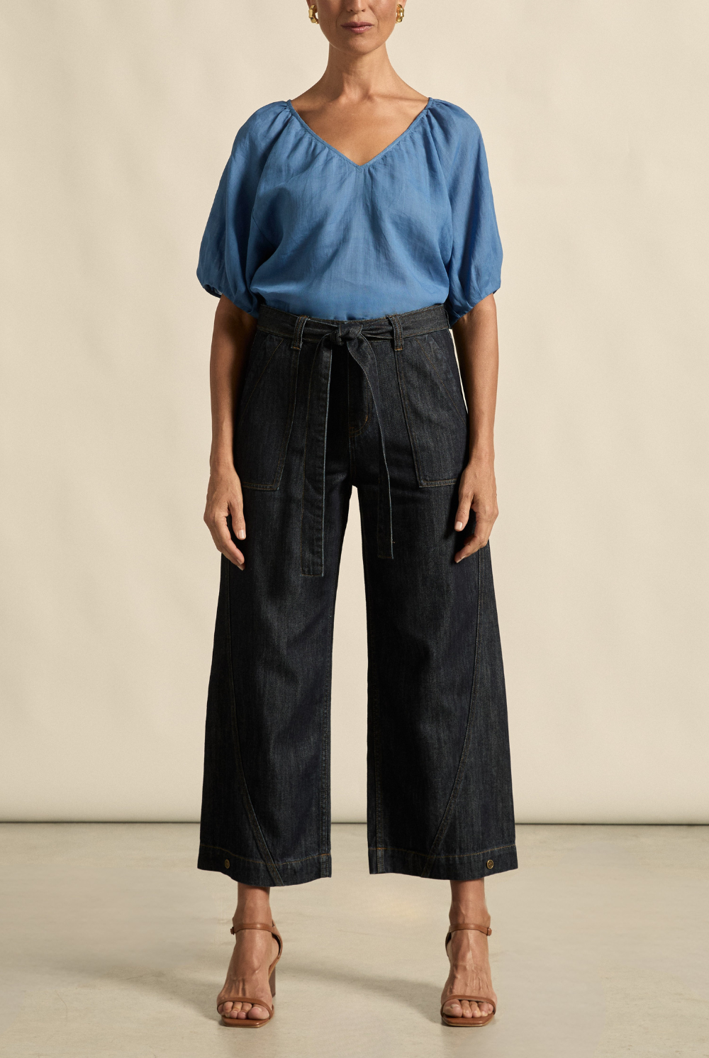 Woman wearing a blue blouse and dark denim wide-leg pants against a beige background