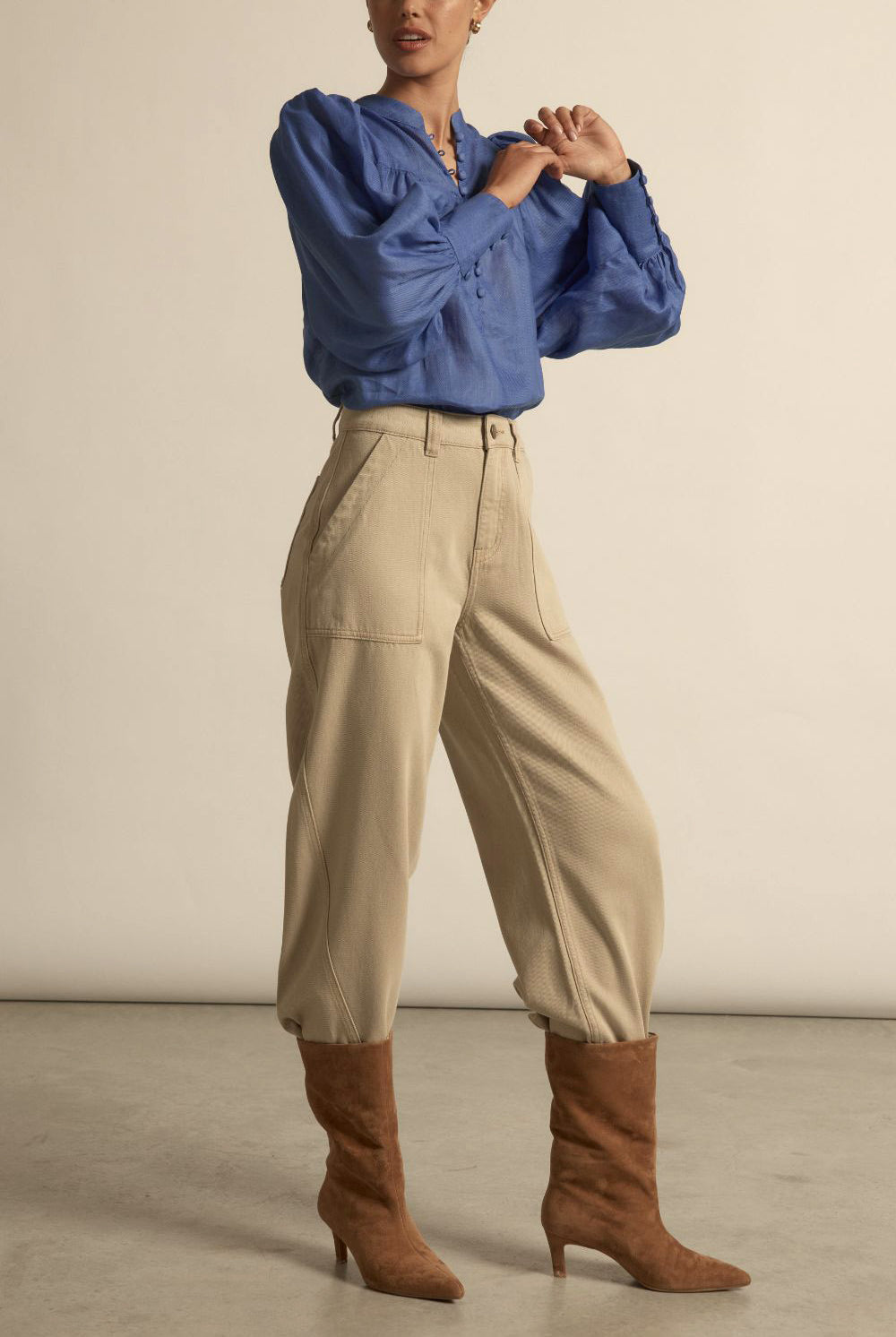 Person wearing a blue blouse, beige pants, and brown boots on a neutral background
