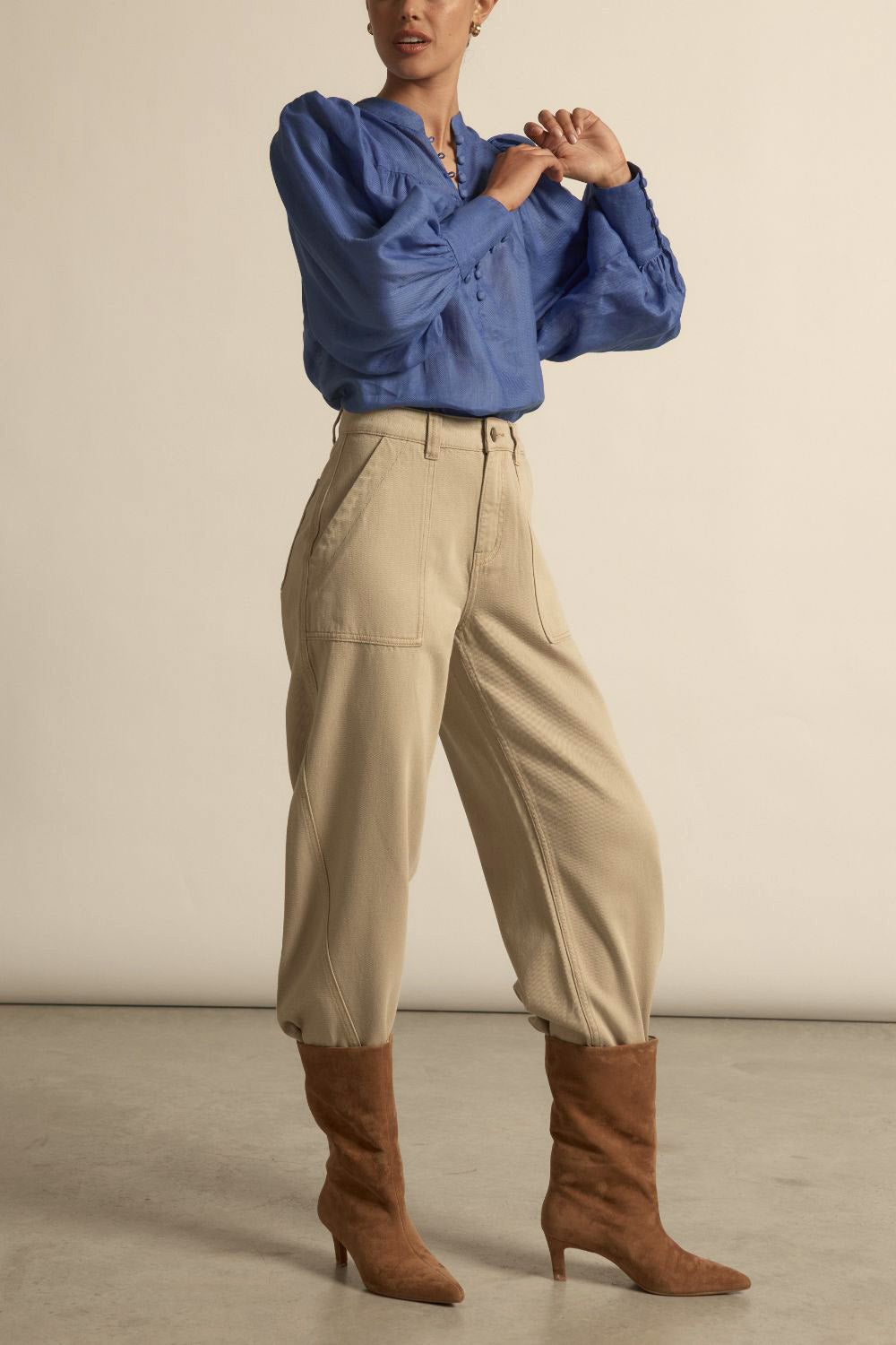 Person wearing a blue blouse, beige pants, and brown boots on a neutral background