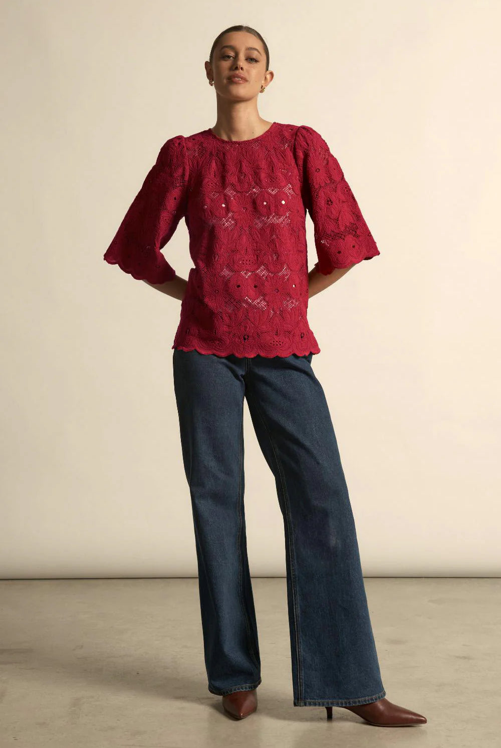 Woman wearing a red blouse with floral patterns and blue jeans against a plain background
