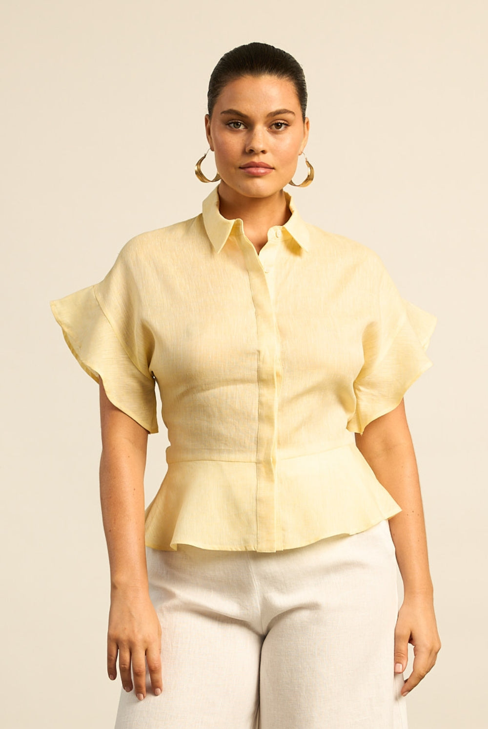 Woman wearing a light yellow blouse with ruffled sleeves on a beige background