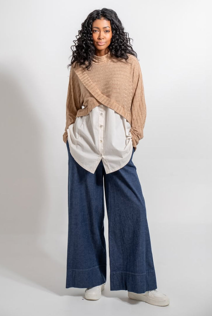 Woman wearing a beige top, white button-up shirt, and blue wide-leg pants on a white background