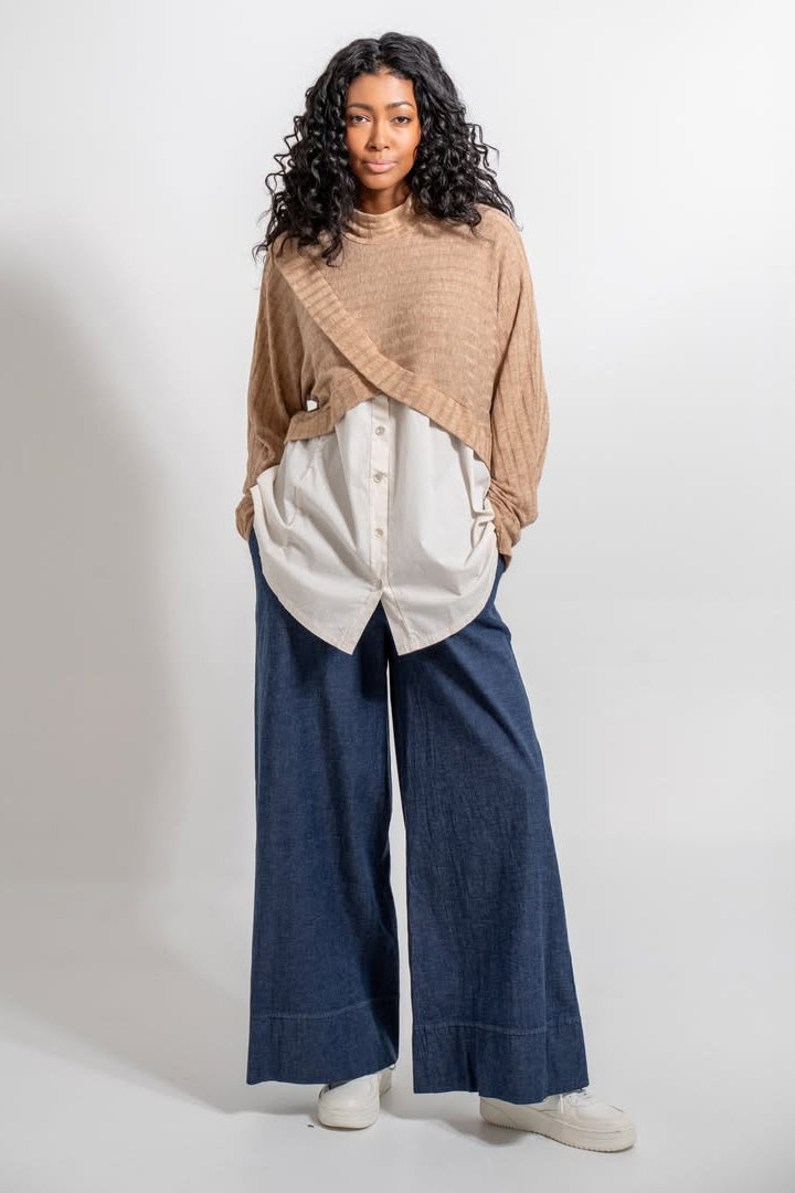 Woman wearing a beige top, white button-up shirt, and blue wide-leg pants on a white background