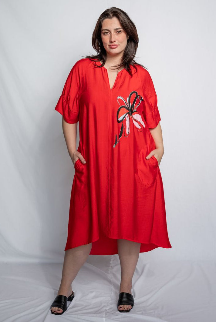Woman wearing a v neck bright red midi length dress with elbow length sleeves and flower motif against a white background.